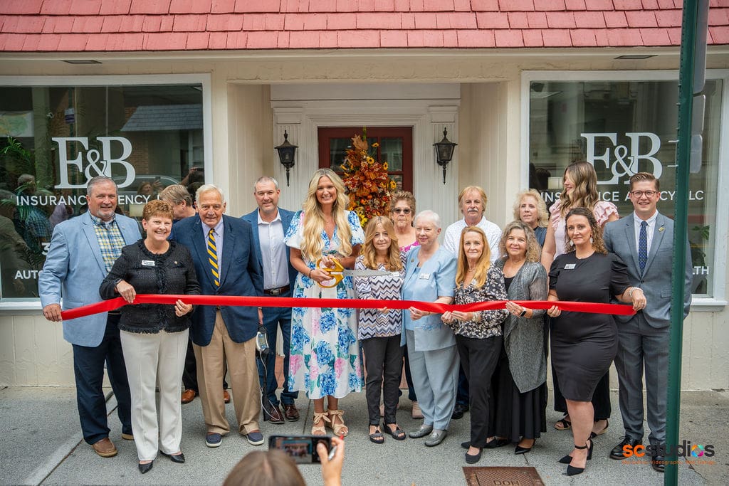 A group of well-dressed professionals and guests gather for a formal ribbon-cutting ceremony at a storefront venue, celebrating what appears to be a business opening or grand reopening.
